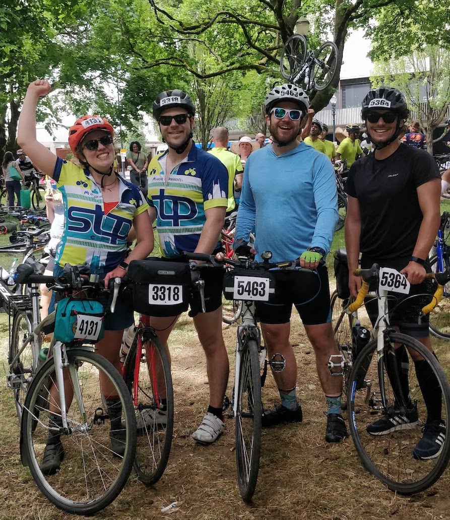 4 young adults, 1 woman and 3 men, posing with their bikes after a long bike ride.