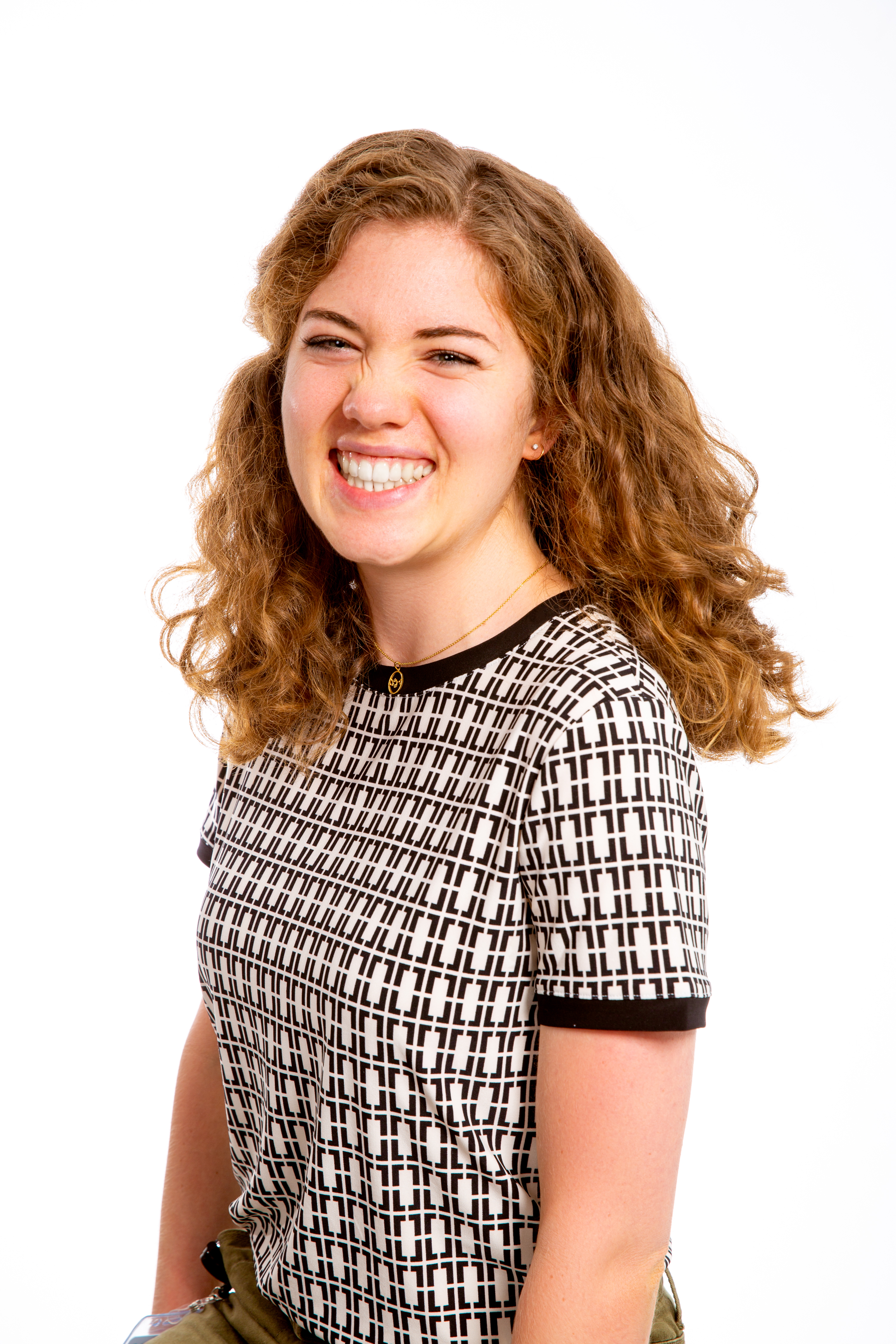 professional headshot photo of Caroline. She is wearing a black and white print shirt, has curly blonde/red hair and is smiling.